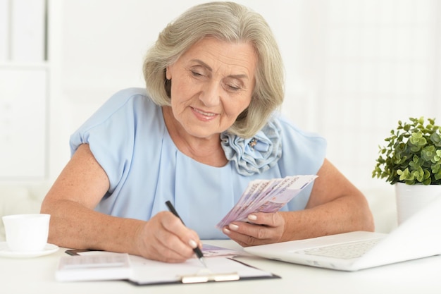 Senior vrouw in koptelefoon zittend aan tafel met laptop