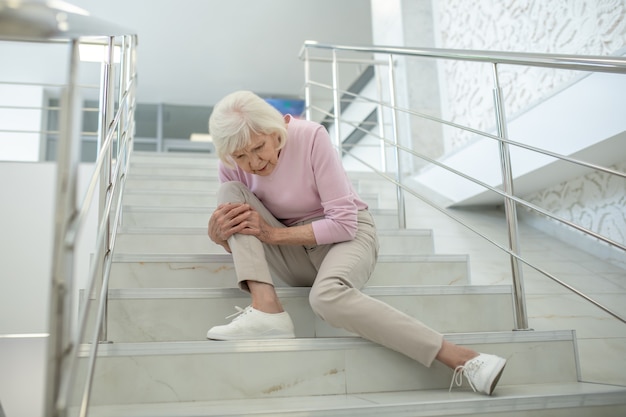 Senior vrouw in roze shirt zittend op de trap met een beschadigde knie