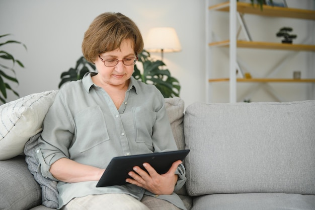Senior vrouw kijkt en lacht om haar digitale tablet op de bank