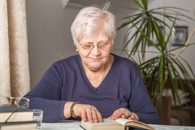 Senior vrouw leest geconcentreerd in een boek in de bibliotheek in het bejaardentehuis