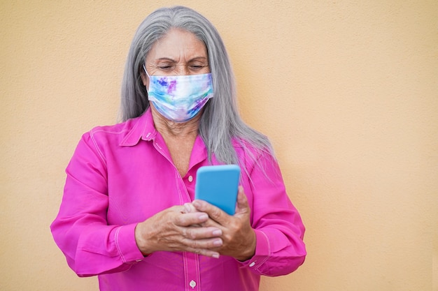 Senior vrouw met behulp van mobiele telefoon terwijl het dragen van beschermend gezichtsmasker