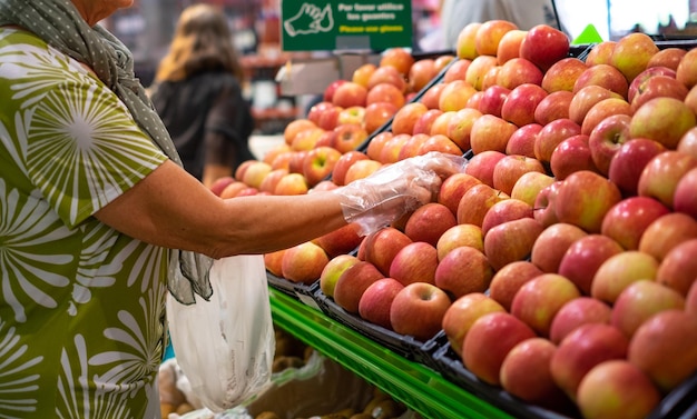 Senior vrouw met beschermende handschoenen verse rode appels selecteren in de voedselafdeling in supermarkt consumentisme concept stijgende prijzen inflatie