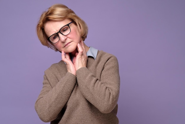 Senior vrouw met een bril die haar lymfeklieren controleert omdat ze bang is om griep te krijgen