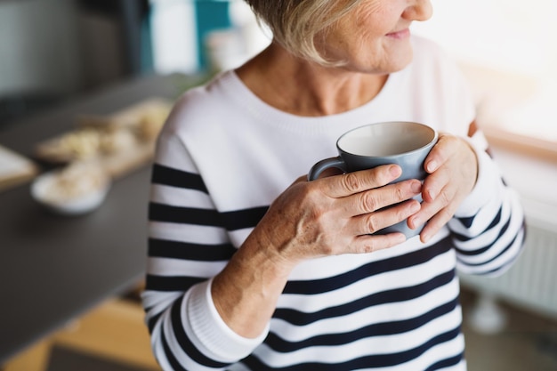 Senior vrouw met een kop koffie in de keuken