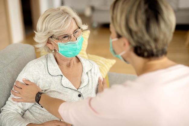 Senior vrouw met gezichtsmasker terwijl ze thuis met haar dochter praat