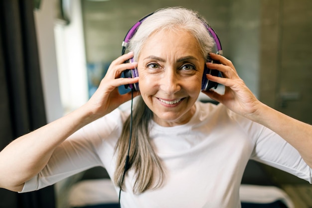 Senior vrouw met grijs haar draagt een koptelefoon die naar de muziek luistert