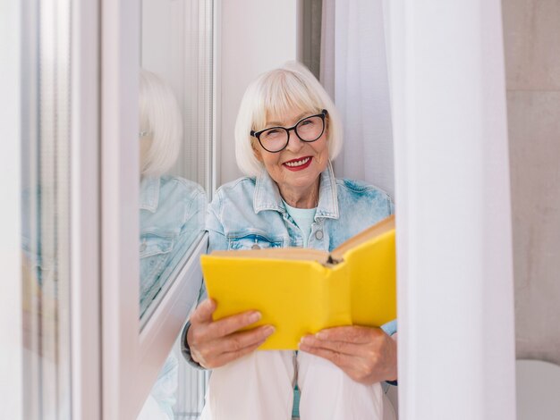 senior vrouw met grijs haar leest een boek bij het raam thuis Onderwijs pensioen anti leeftijd