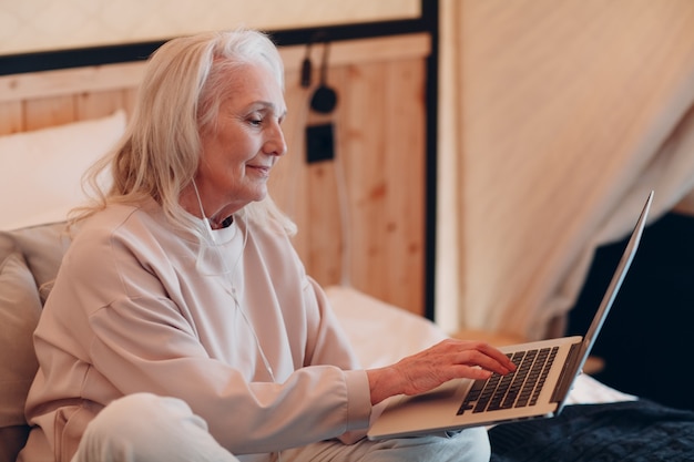 Senior vrouw met laptop ontspannen op glamping camping tent. moderne vakantie levensstijl concept.