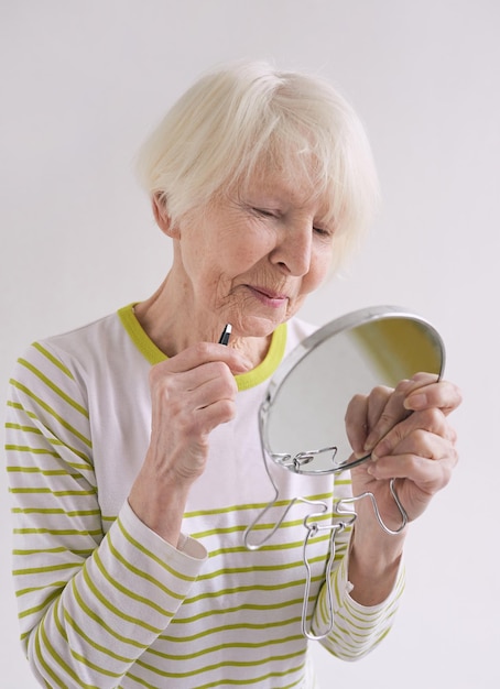 Senior vrouw met wenkbrauwpincet en kleine spiegel die haar baard plukt