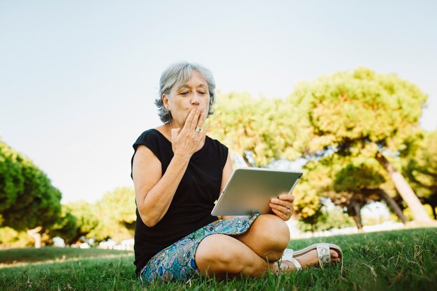 Senior vrouw online chatten met zijn tablet in een park