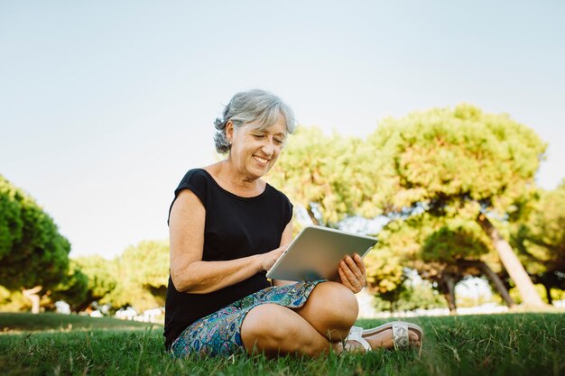 Senior vrouw online chatten met zijn tablet in een park