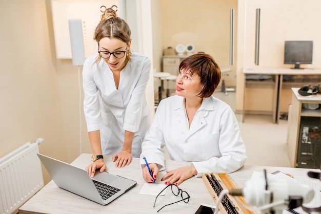 Senior vrouw oogarts met jonge vrouwelijke assistent die met laptop op kantoor werkt