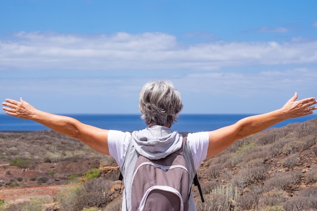 Senior vrouw reiziger genieten van buiten wandelen, kijkend naar de horizon over zee met open armen