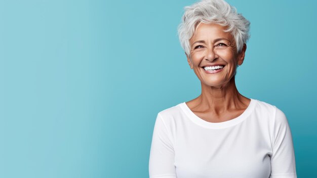 Senior vrouw staande voor de camera in wit T-shirt geïsoleerd op blauwe achtergrond