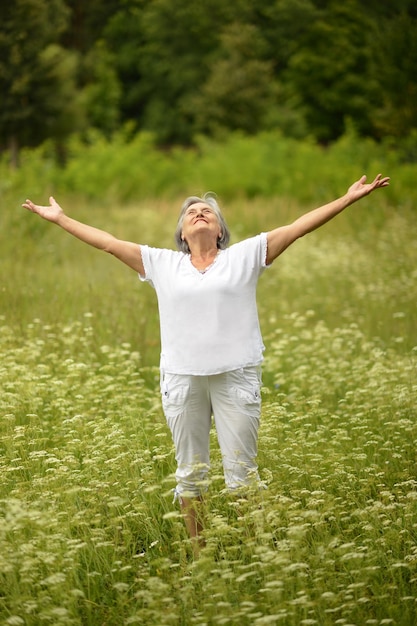 Senior vrouw stond met open armen in veld met wilde bloemen