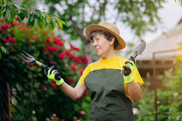 Senior vrouw tuinman in een hoed die in haar tuin werkt met uitrustingsstukken Het concept van tuinieren, groeien en zorgen voor bloemen en planten