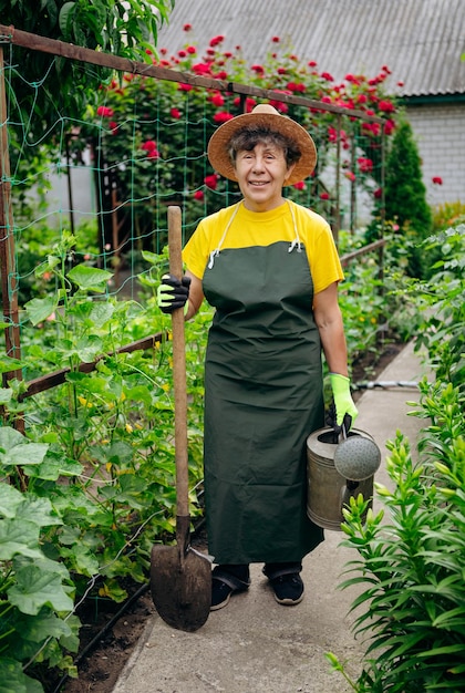 Senior vrouw tuinman in een hoed die in haar tuin werkt met uitrustingsstukken Het concept van tuinieren, groeien en zorgen voor bloemen en planten