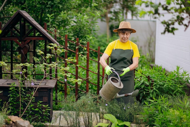 Senior vrouw tuinman in een hoed die in haar tuin werkt met uitrustingsstukken Het concept van tuinieren, groeien en zorgen voor bloemen en planten