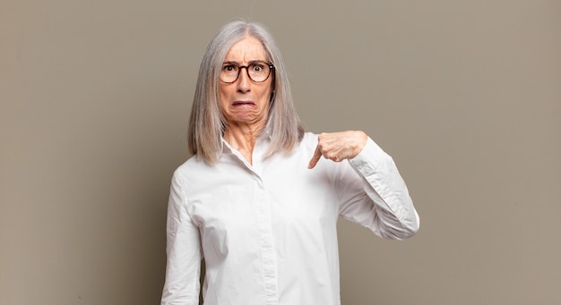 Senior vrouw voelt zich verward, verbaasd en onzeker, wijst naar zichzelf, vraagt zich af en vraagt wie, ik?