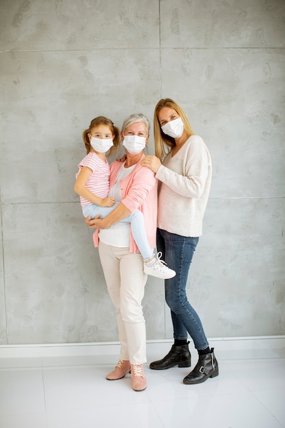 Senior vrouw, volwassen vrouw en schattig klein meisje, drie generaties met beschermende gezichtsmaskers thuis