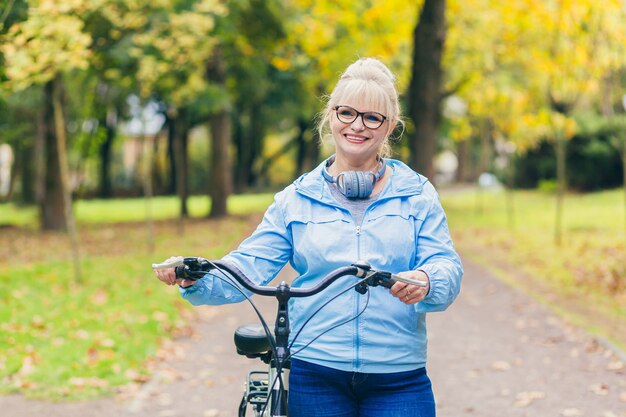 senior vrouw wandelen in het park met een fiets, zonnige dag