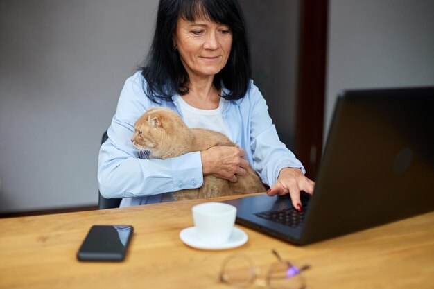 Senior vrouw werkt aan een notebook, laptop en houdt kat vast