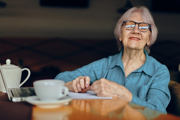 Senior vrouw zit in een café met een kopje koffie en een laptop Gepensioneerde vrouw chat ongewijzigd