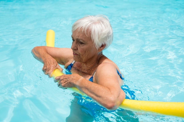 Senior vrouw zwemmen met opblaasbare buis in het zwembad