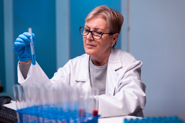 Senior wetenschapper die een monster met chemicaliën in een reageerbuis opneemt met handschoenen en een beschermende bril