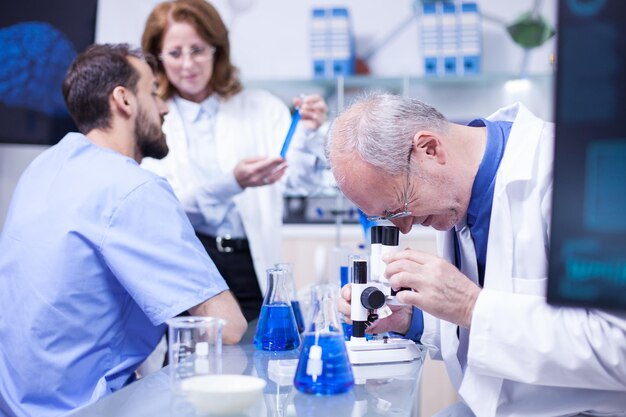 Senior wetenschapper doet testen onder de microscoop in een modern laboratorium. Team van wetenschapper die op de achtergrond werkt.