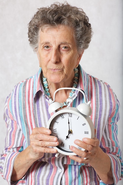 Senior woman between 70 and 80 years old shows vintage alarm clock