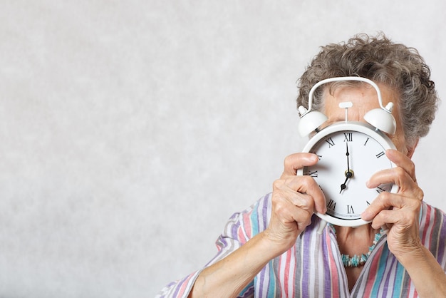 Senior woman between 70 and 80 years old shows vintage alarm clock