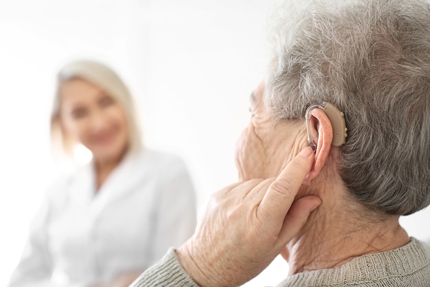 Senior woman adjusting hearing aid on light , closeup