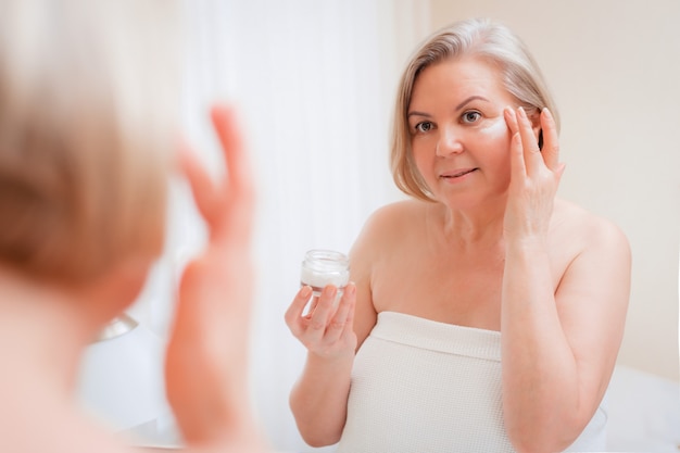 Photo senior woman applying cream on her face