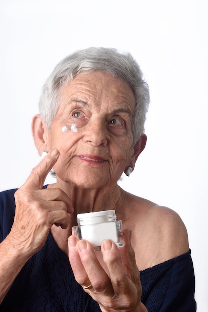 Пожилая женщина наносит на лицо крем или увлажняющий крем