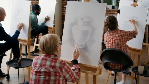 Senior woman attending art class lesson to develop new skills, learning to draw vase model on canvas. Elder student drawing artistic sketch to practice personal growth in workshop.