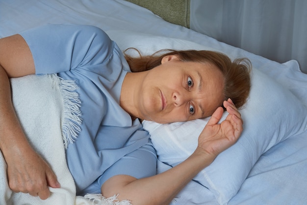 Senior woman in blue pajamas lying in bed suffering from\
insomnia