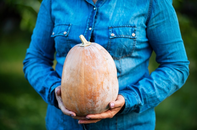 Senior woman in a blue shirt holds a pumpkin in the garden