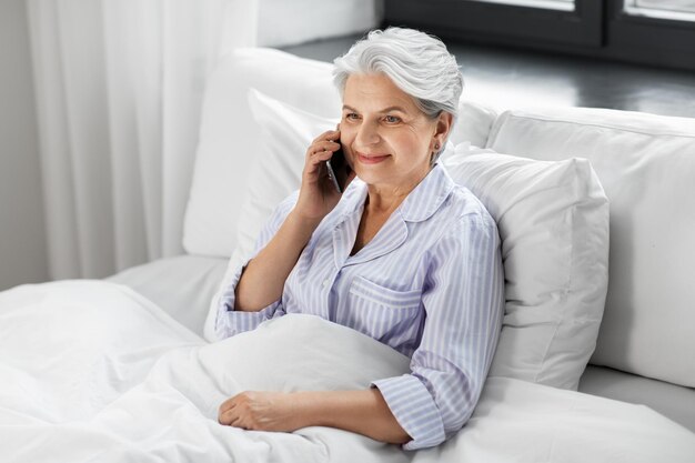 senior woman calling on smartphone in bed at home