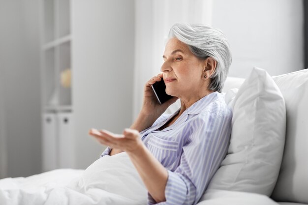 senior woman calling on smartphone in bed at home