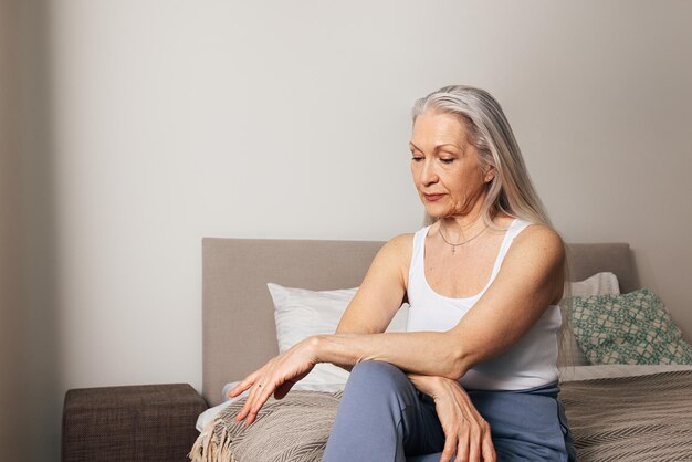 Senior woman in casuals sitting on bed and looking down Sad female is sitting in her bedroom