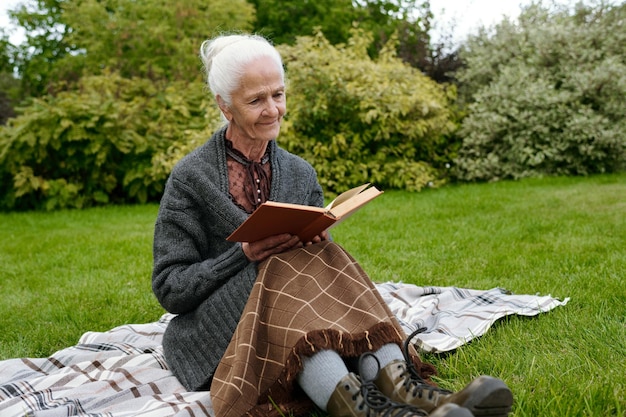 Senior woman in casualwear sitting on checkered woolen plaid and reading