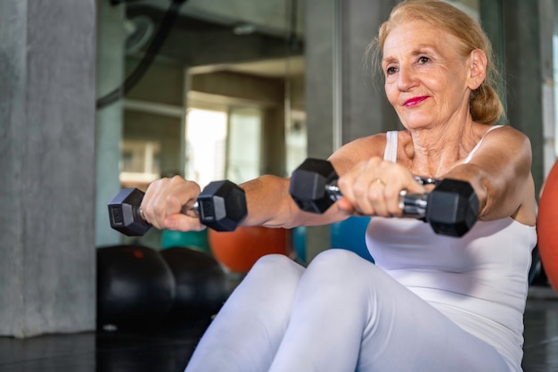 Braccio di addestramento caucasico della donna senior con dumbell alla palestra di forma fisica.