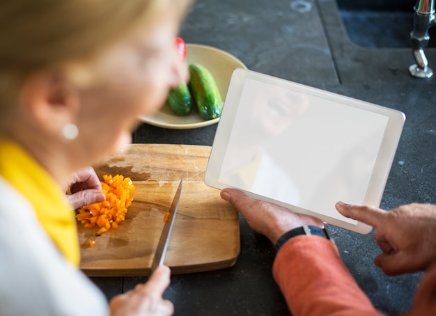 Donna maggiore che cucina la compressa della cucina dell'alimento