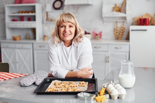 La donna senior cucina i biscotti di natale sulla cucina durante il giorno