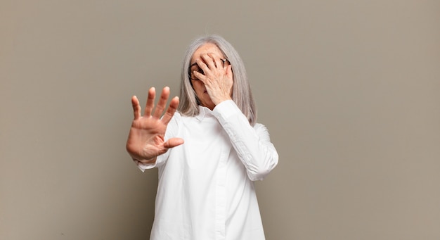 Donna anziana che copre il viso con la mano e mette l'altra mano davanti per fermare la fotocamera, rifiutando foto o immagini