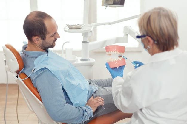 Senior woman dentist explaining tooth surgery using plaster model of mandible