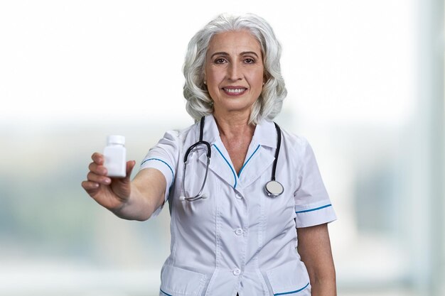 Senior woman doctor looking at camera and offering pills.