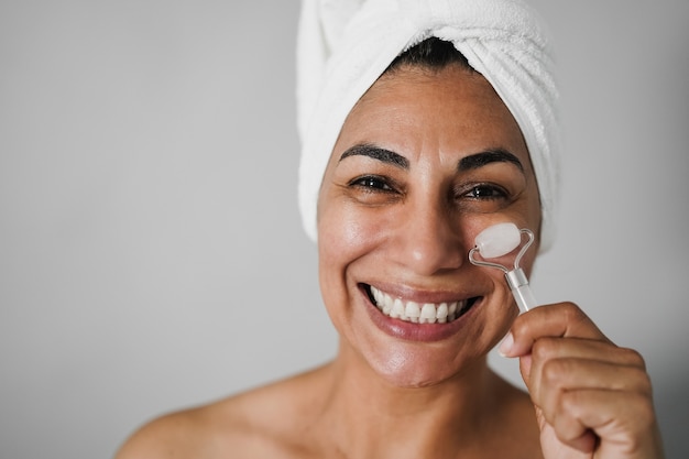 Senior woman doing skin care treatment using face roller - main focus on eyes