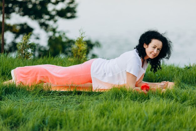 Donna senior che fa la plancia di asana di yoga all'aperto e che guarda ... yoga